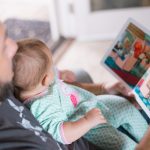 person carrying baby while reading book